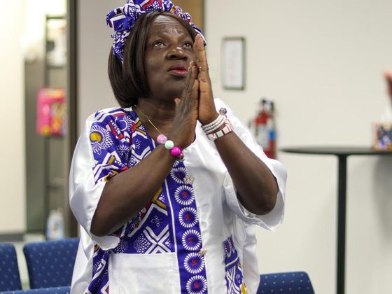 A woman in a headwrap praying with her hands clasped.