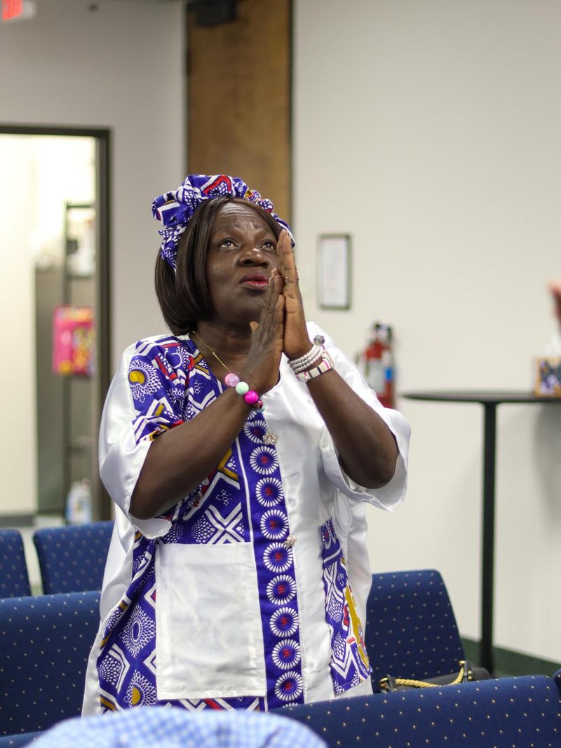 A woman in a headwrap praying with her hands clasped during the service.