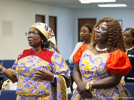 Three women of the Women's Movement worshipping together in patterned dress.