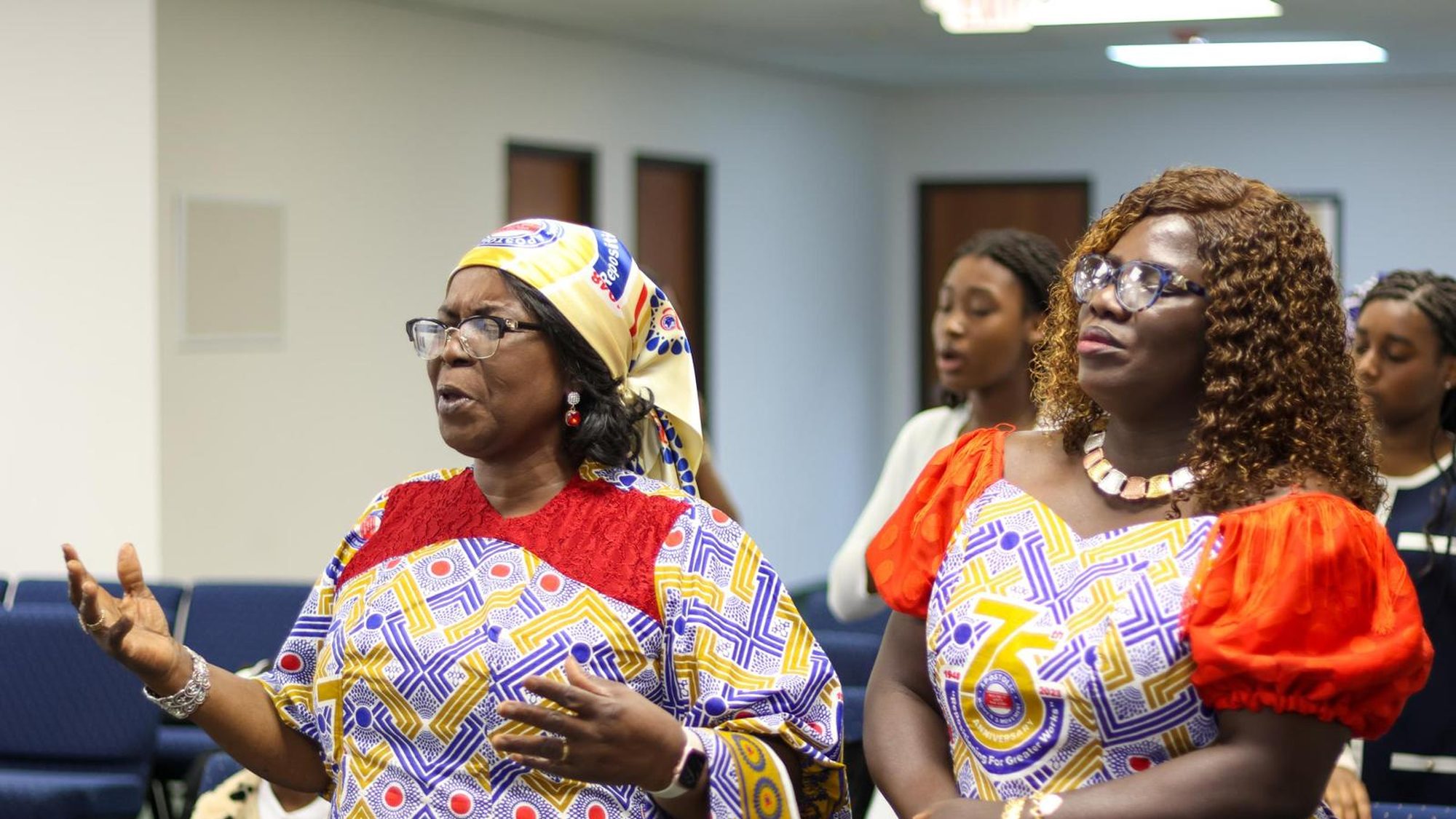 Three women of the Women's Movement worshipping together in patterned dress.