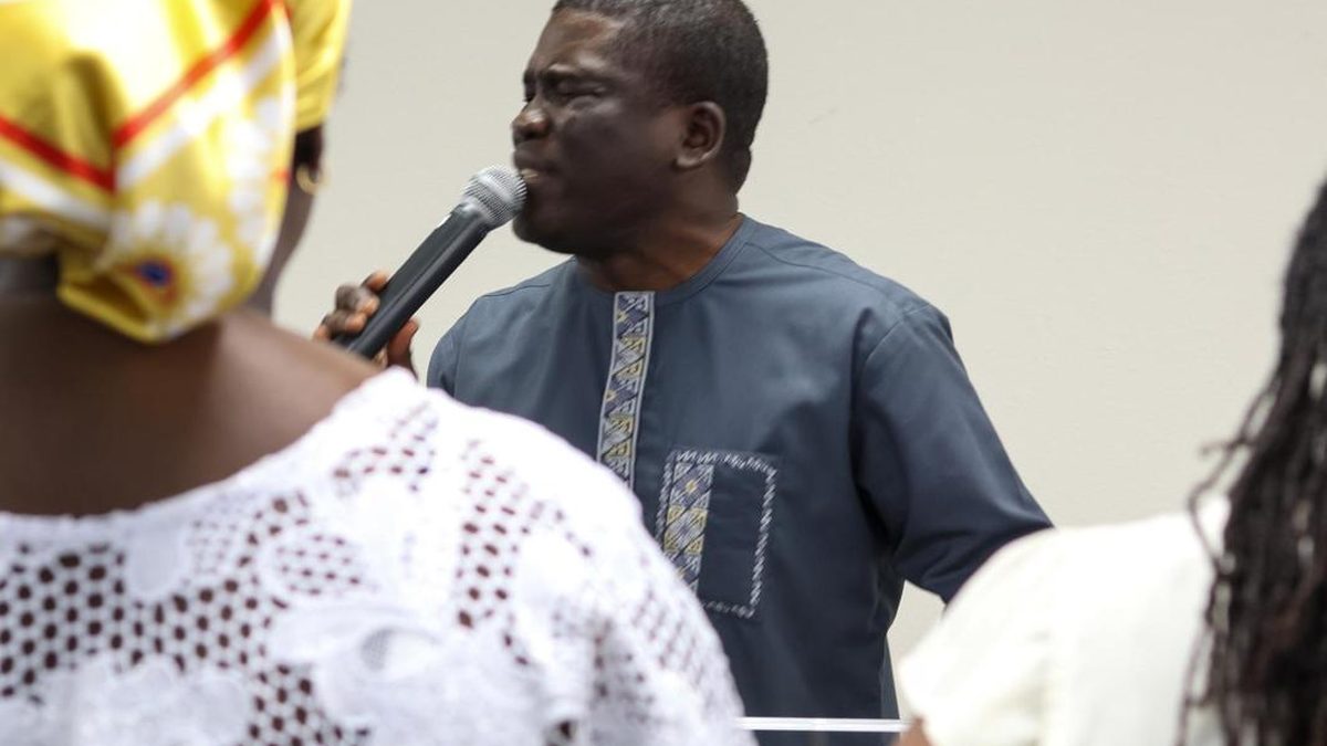 A church leader praying over members of the congregation with a microphone in hand.