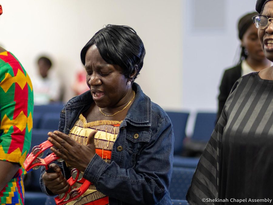 A woman worshipping with her eyes closed, surrounded by the congregation.