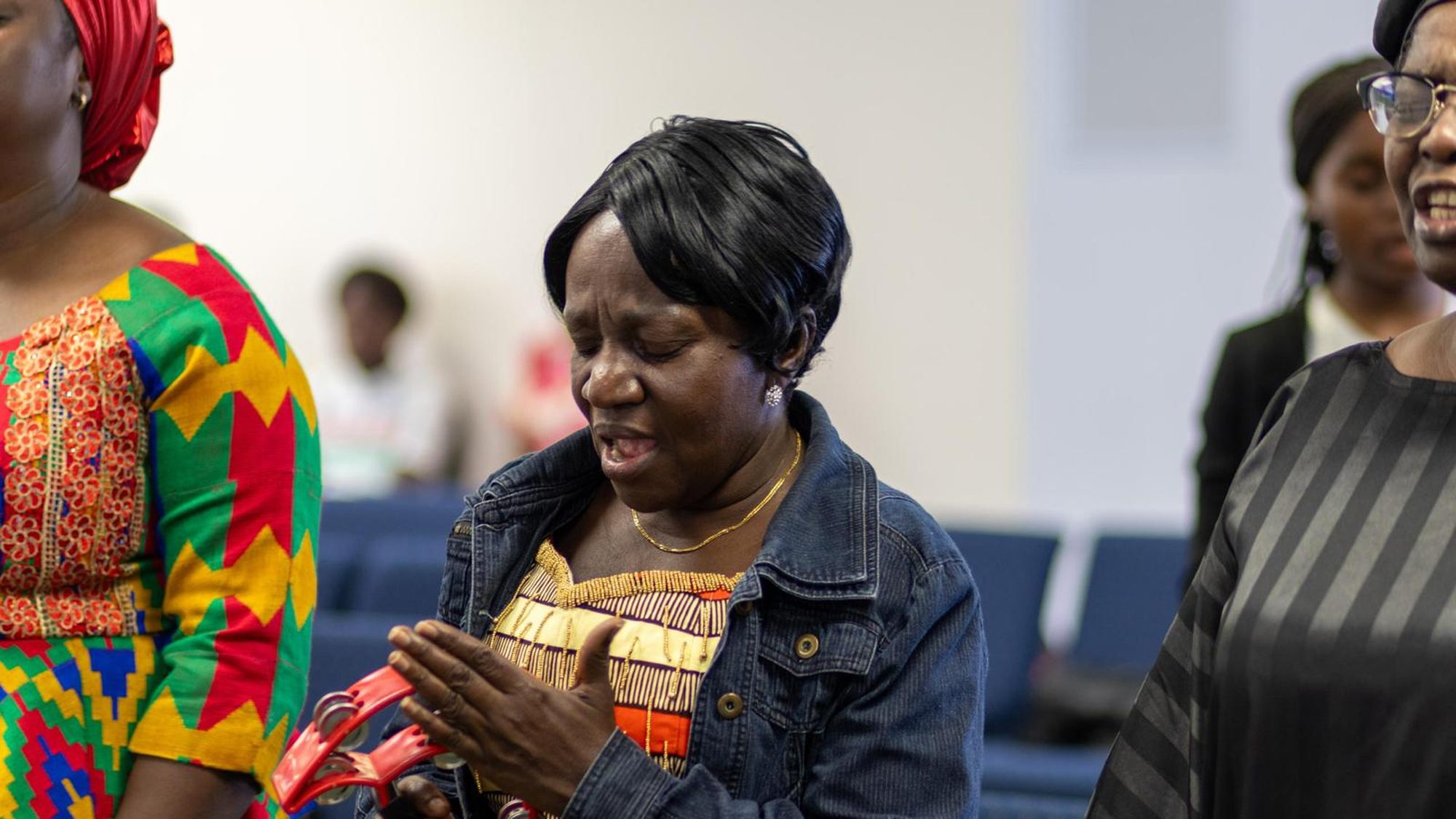 A woman worshipping with her eyes closed, surrounded by the congregation.