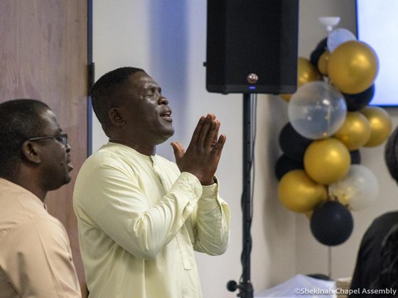 Two men standing side by side with hands raised in prayer.