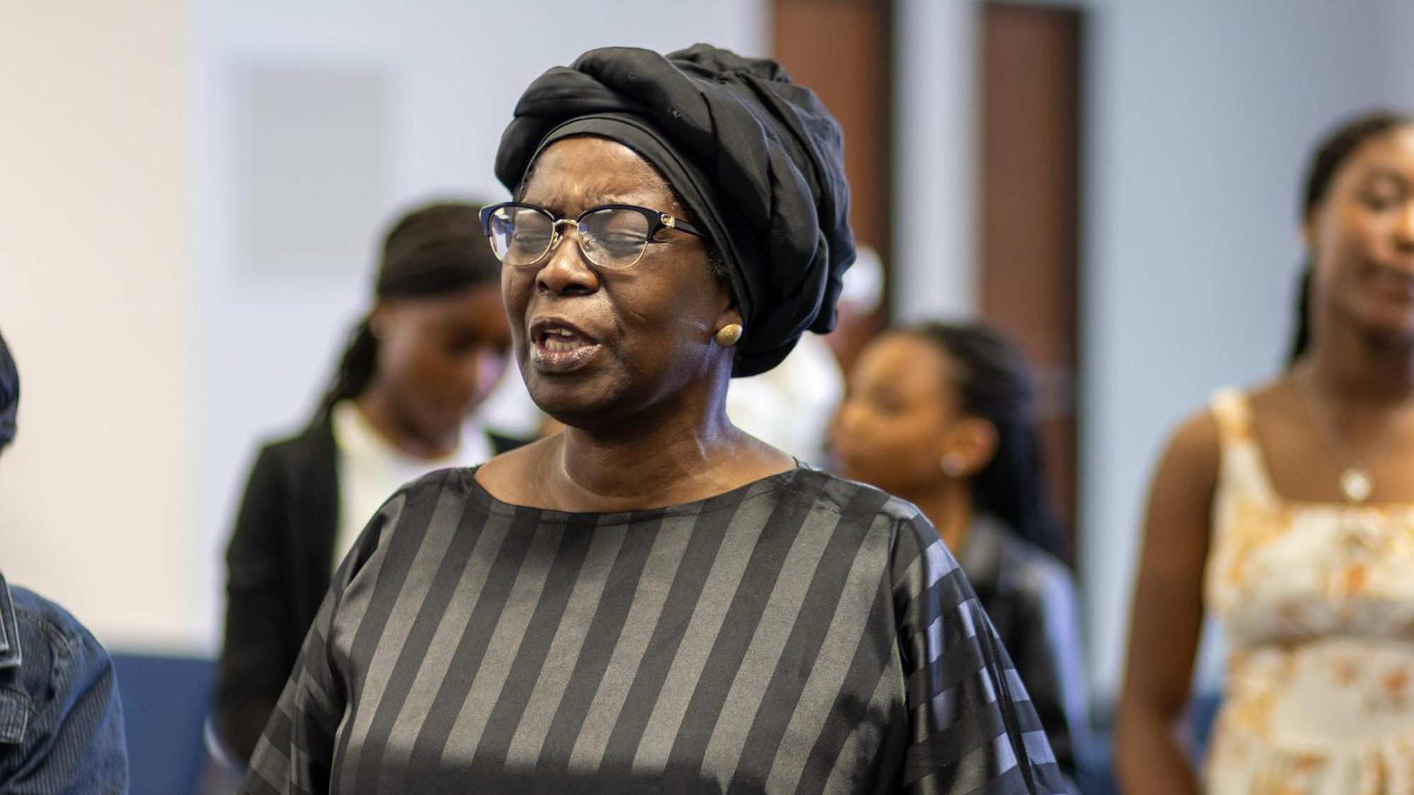 An elder of the church worshipping, with the congregation standing behind her.