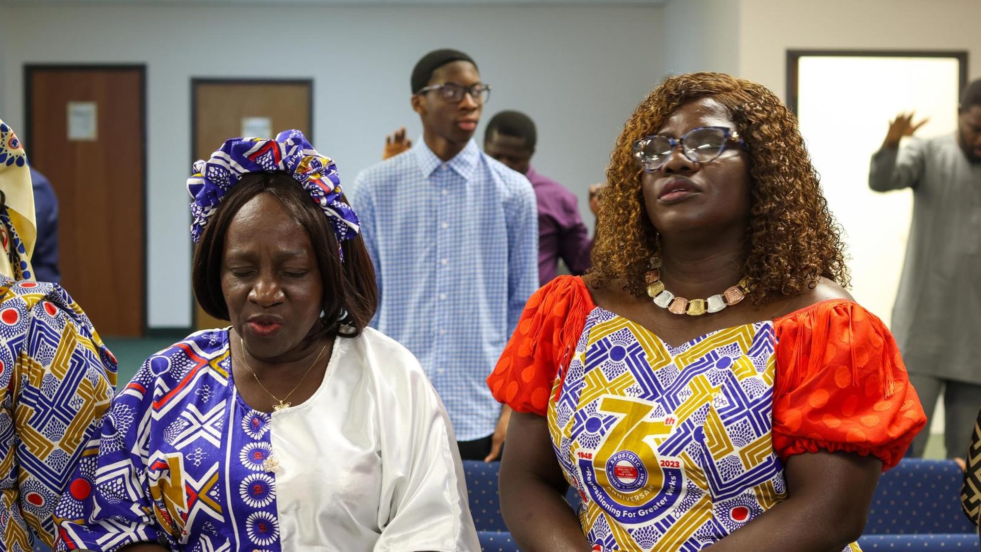 Members of the congregation standing together in worship on a Sunday morning, many in colourful West African dress.